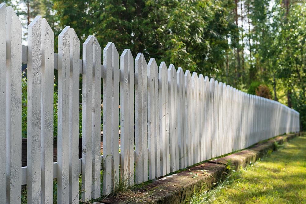 white picket fence on edge of backyard - types of fences concept
