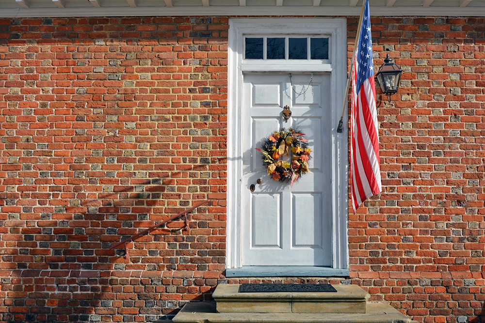 brick house with white wooden door and american flag - autumn wreath on the door - front door concept